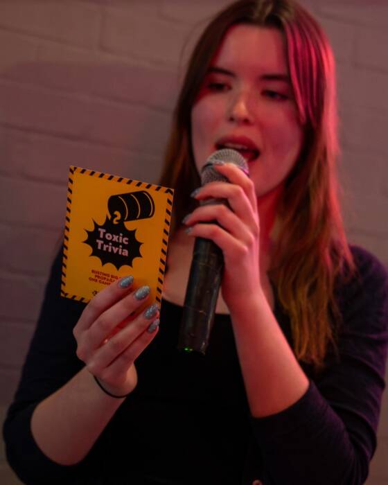 A young woman holding a Toxic Trivia card