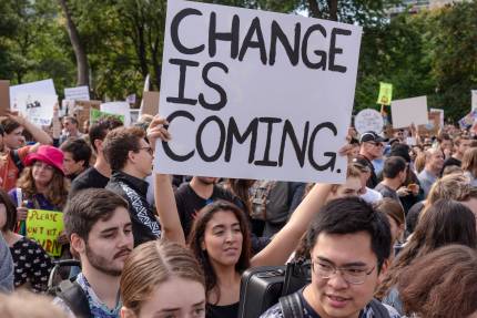 A young woman holding a sign that reads "Change is Coming"