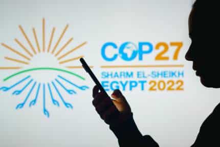 Mujer sostiene un smartphone con el logotipo de la Conferencia de las Naciones Unidas sobre el Cambio Climático COP27 en segundo plano