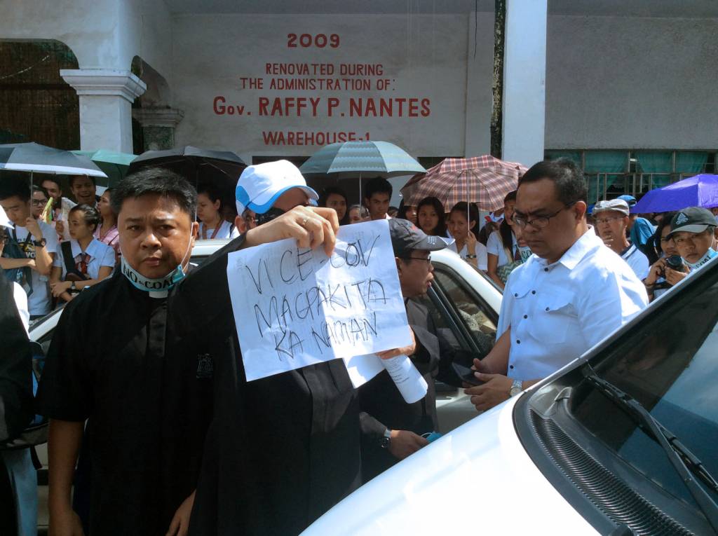 Fr. Raul Enriquez holds a banner that reads: "Vice-Governor show yourself". In front of the vehicle that carries the vice governor. Photo: Fread De Mesa