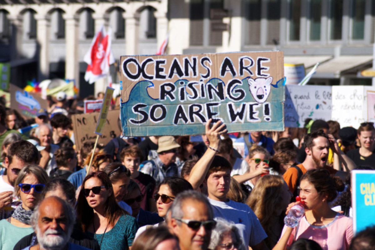 group of protestors with a sign that reads, oceans are rising. So are we!