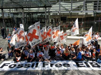 Group of activists outside European Investment Bank headquarters carrying banners and flags calling for an end to fossil fuel finance