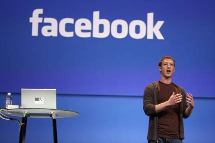 Picture of Mark Zuckerberg next to podium in front of Facebook logo on blue background