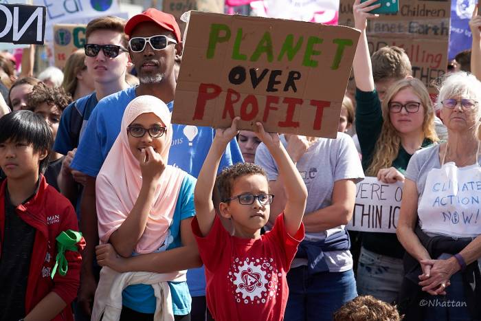 A young boy hold a sign that reads: People Over Profit