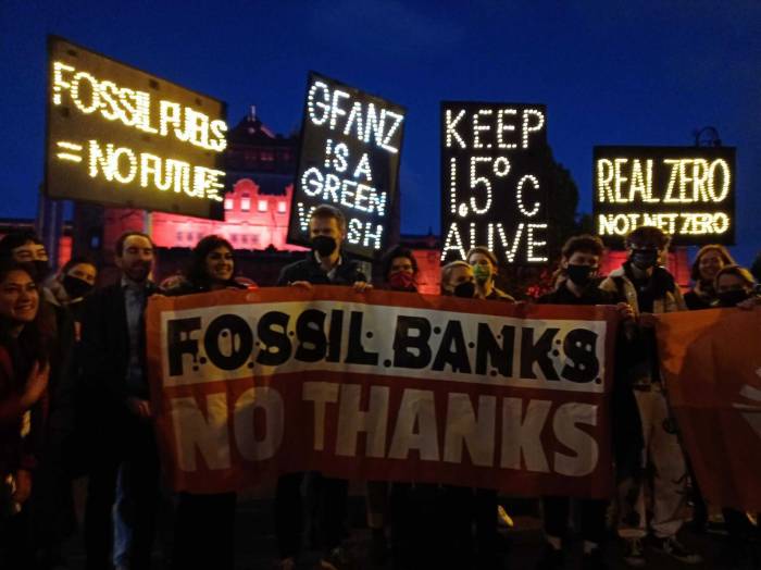 Activists hold signs protesting fossil finance outside COP26