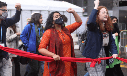 A woman in an orange sari is holding a red line, fist raised, during the final day of COP26