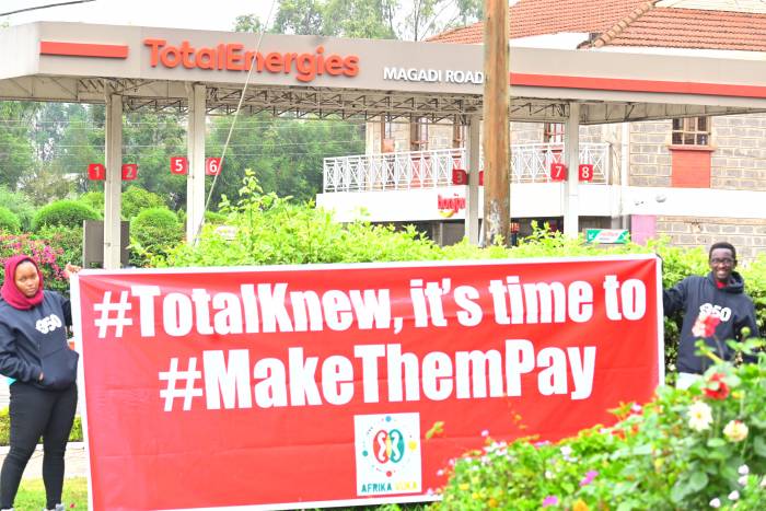 Activists stand outside a Total gas station in Nairobi with a sign that says "#TotalKnew, it's time to #MakeThemPay." 