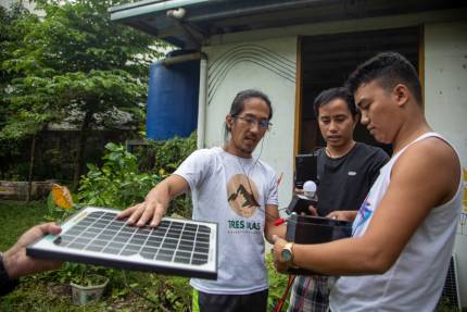 Three men construct a portable solar planel during a community-centred energy project in Tacloban, Philippines