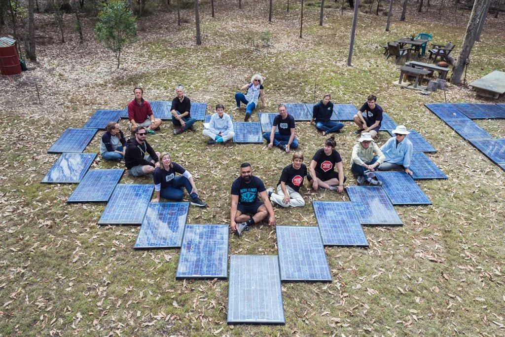 Several people sitting within a heart formed by solar panels, during an community-centred energy action.