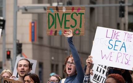 Students protesting and holding up signs saying "divest," and "like the sea, we rise."