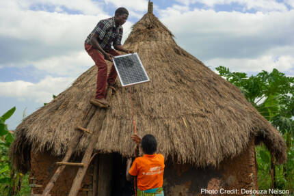 REPower Afrika community members in Uganda install a solar panel on a thatched-roof home.