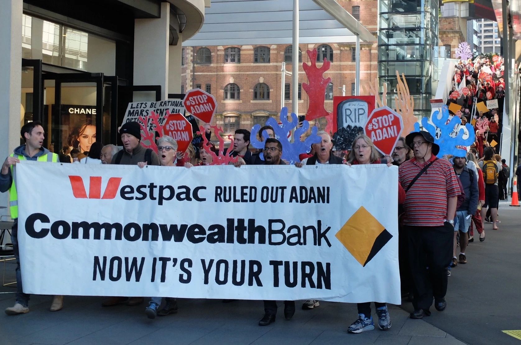 Protesters raise signs urging Adani to stop the coal mine project. Sydney, Australia